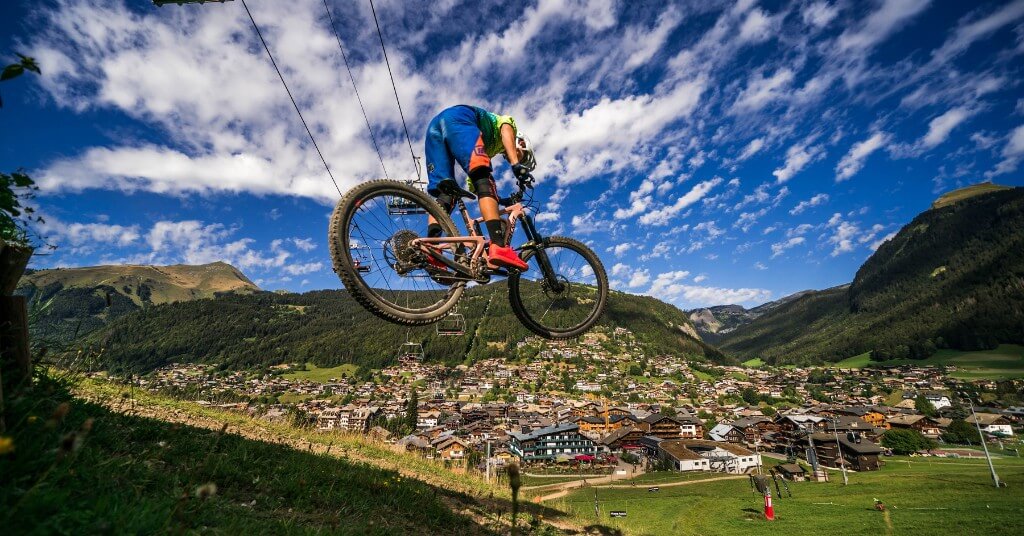 Vététiste effectuant un saut avec le village de Morzine en arrière-plan